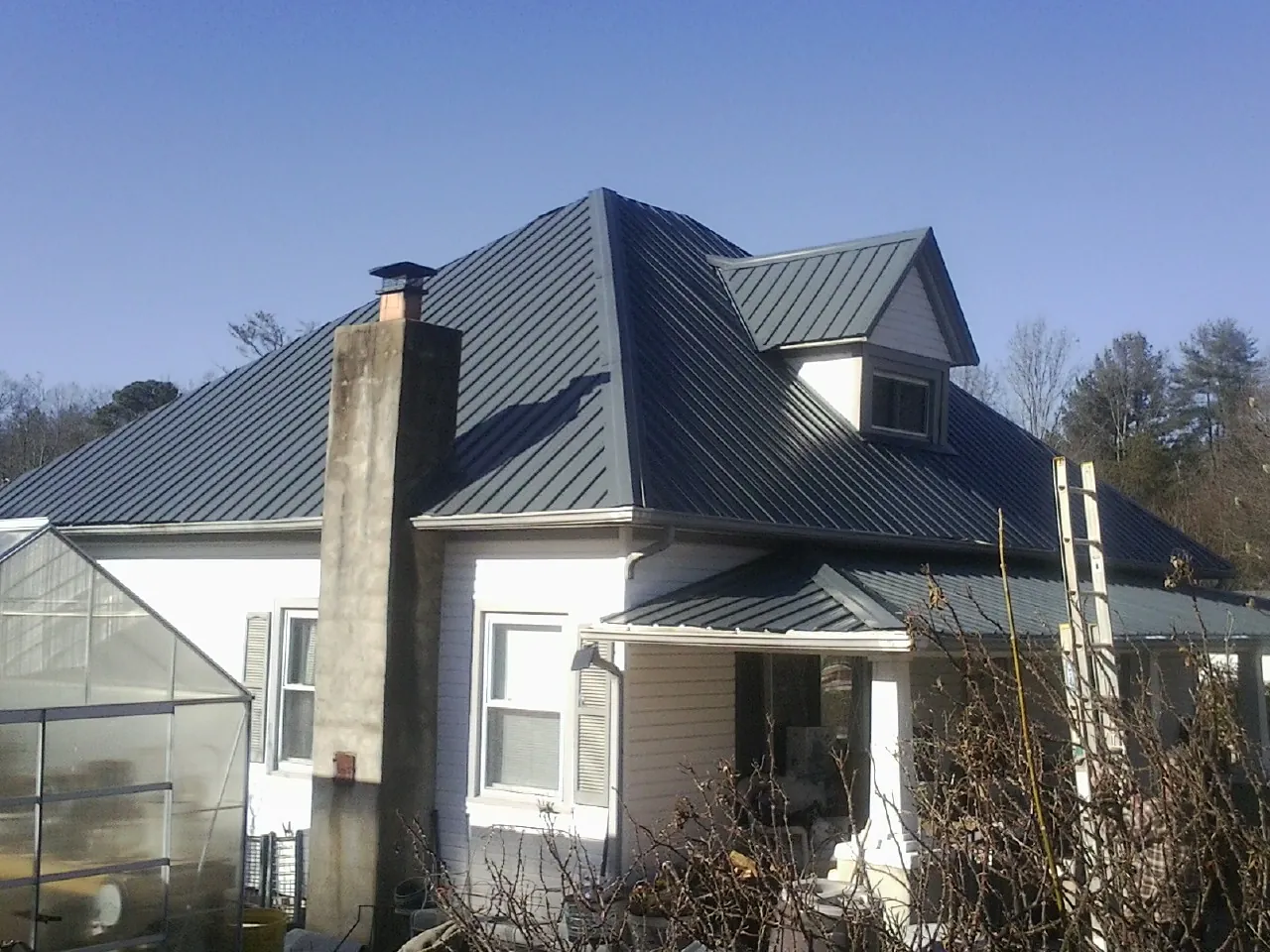 Dark blue standing seam metal roof on a white farmhouse with dormer — Slate & Tile Roof Repair by Roofing Brothers in Richland Center