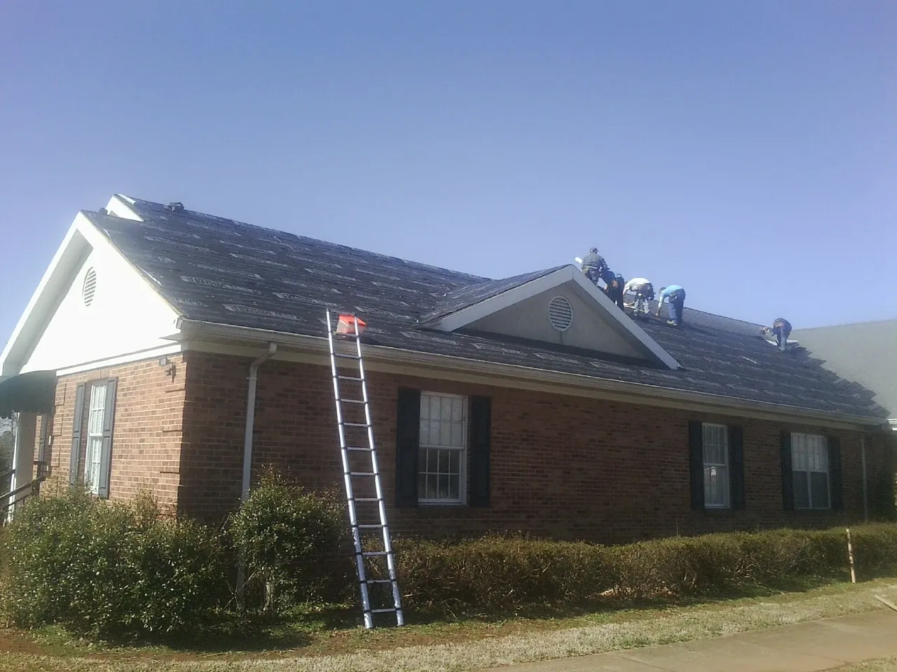 Crew tearing shingles off a brick ranch roof with a ladder set — Metal Roof Repair work by our crew in Richland Center