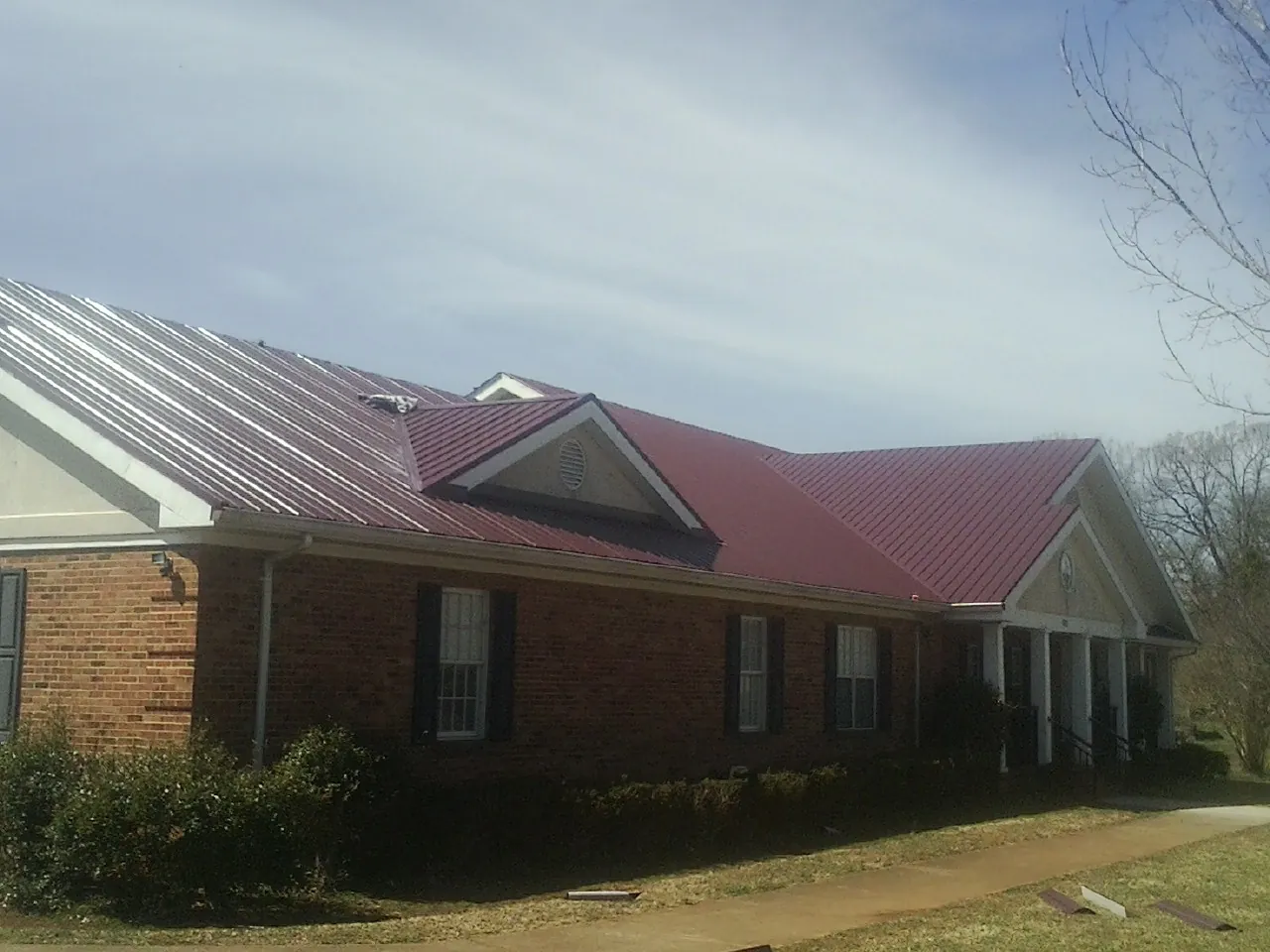 Red metal roof with gabled entries on a long brick building, from a Hail Damage Roof Repair job in Richland Center
