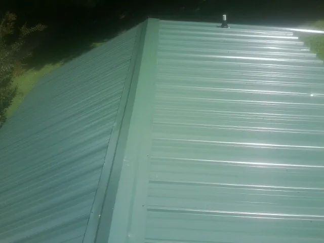 New green metal panels meeting at the ridge of a roof — Flat Roof Repair work by our crew in Richland Center