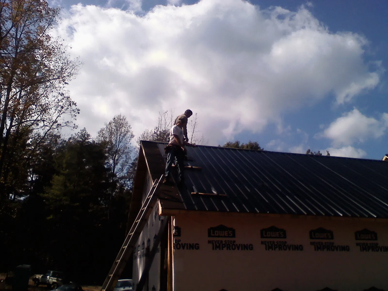 Roofer fastening dark metal panels high against a cloudy sky, from a Roof Inspection job in Richland Center