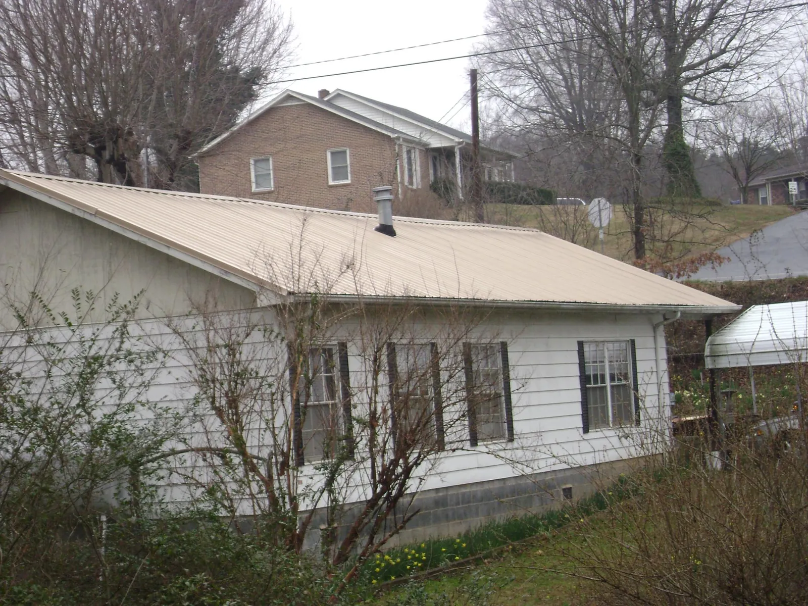 Tan metal roof on a white sided house set into a hillside — Commercial Roofing by Roofing Brothers in Richland Center
